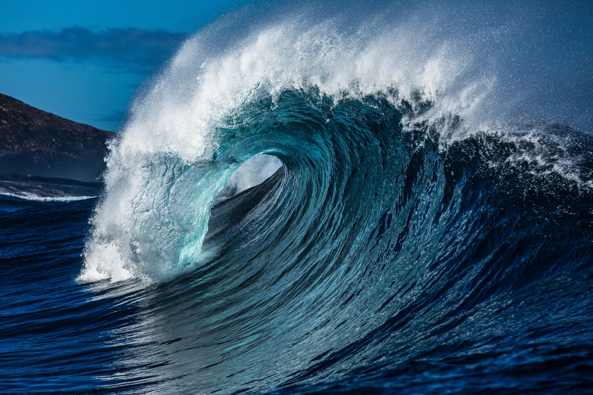 Large blue wave with perfect curl breaking in the open ocean over a shallow reef bombora